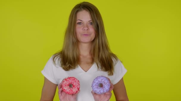 Mulher em uma camiseta branca levanta as mãos com donuts azuis e vermelhos, sorrisos — Vídeo de Stock