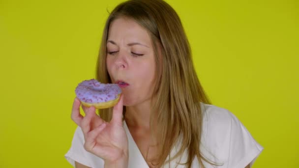 Vrouw in een wit T-shirt bijt, eet een heerlijke blauwe donuts, geniet van de smaak — Stockvideo