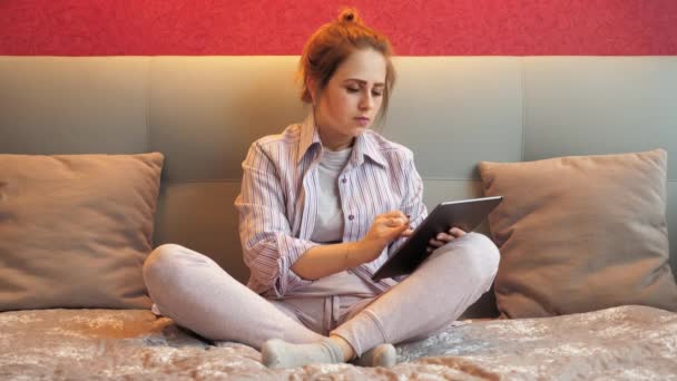 Mujer cansada en casa sentada en la cama utiliza la tableta para el trabajo y se duerme — Vídeos de Stock