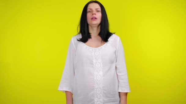 Сердита молода вагітна жінка з чорним волоссям у білій блузці на жовтому тлі — стокове відео