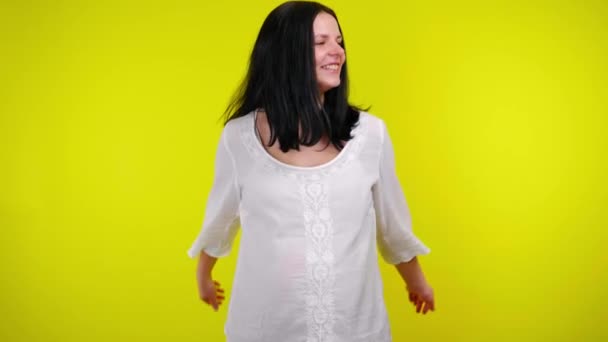 Радостная молодая беременная женщина в белой блузке смеется на желтом фоне — стоковое видео