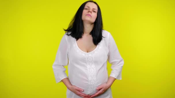 Усталая беременная женщина с черными волосами в белой блузке массирует живот руками — стоковое видео
