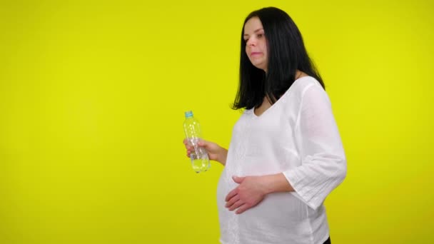 Zwangere vrouw staat met water in een plastic fles en massages maag — Stockvideo