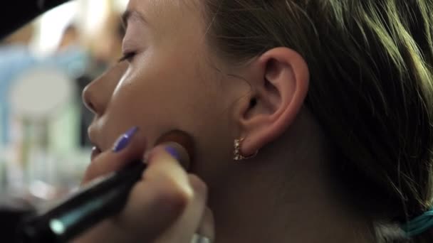 Makeup artist applicerar foundation i ansiktet med borste på tonårstjej i salongen — Stockvideo