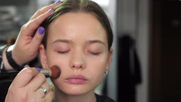 Make-up kunstenaar brengt stichting op gezicht met borstel naar tiener meisje in salon — Stockvideo