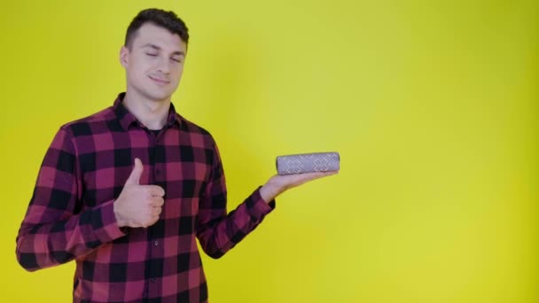 Hombre guapo con caja de regalo en la palma muestra como y sonríe sobre fondo amarillo — Vídeos de Stock