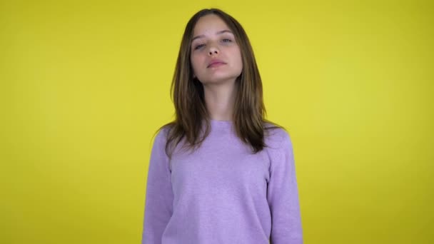 Серйозна дівчина-підліток в рожевому светрі дивиться на камеру на жовтому тлі — стокове відео