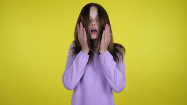 Tiener meisje heft hoofd en geschokt zet handpalmen op wangen op een gele achtergrond — Stockvideo