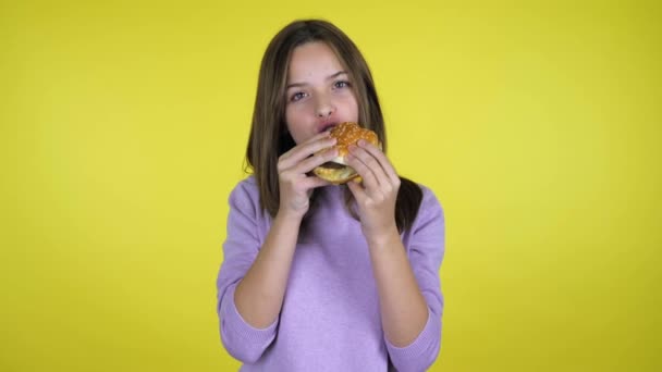 Adolescente chica come una hamburguesa y es infeliz con el sabor en el fondo amarillo — Vídeo de stock
