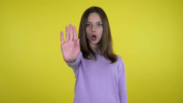 Teenager girl raises her hand with a palm and says stop on yellow background — Stock Video