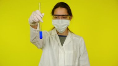Beyaz elbiseli kadın, koruyucu maske test tüpünün içindekileri inceliyor.