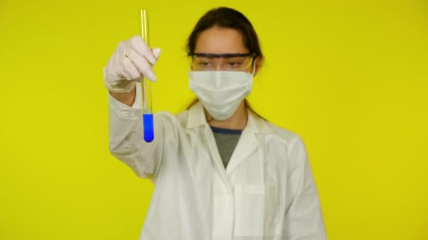 Femme en robe médicale blanche, masque protecteur examine le contenu de l'éprouvette — Video