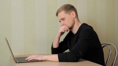 Düşünceli adam bir masada dizüstü bilgisayarla oturuyor.