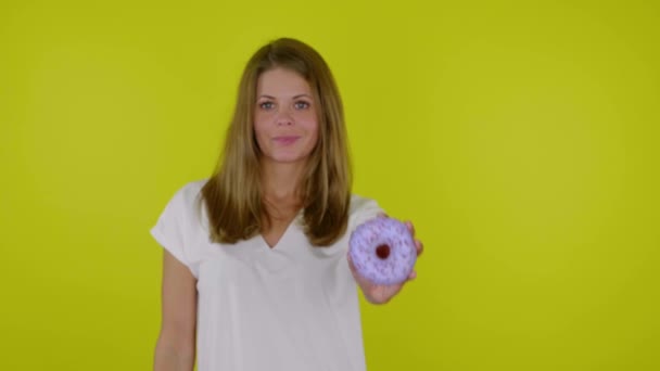 Жінка в білій футболці піднімає руку з синіми пончиками в камеру, посміхається — стокове відео
