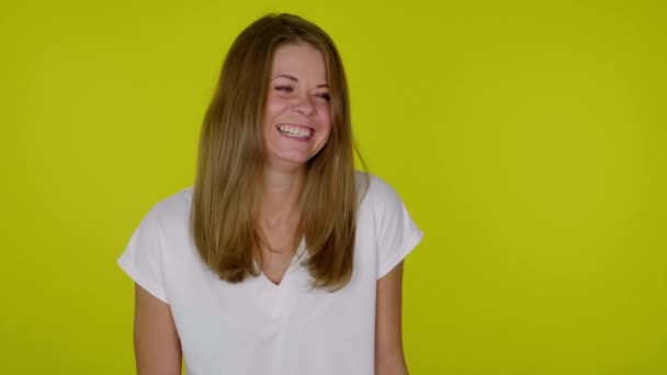 Mujer con una camiseta blanca se ríe, cubre la cara con una palma sobre un fondo amarillo — Vídeo de stock