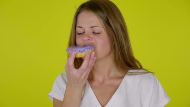 Mujer con una camiseta blanca muerde, come una deliciosa rosquilla azul, disfruta del sabor — Vídeo de stock