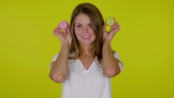 Femme lève les mains avec des macarons roses et jaunes, souriant et posant — Video