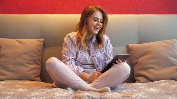 Frau sitzt mit Tablet auf dem Bett, telefoniert mit Video und lacht — Stockvideo