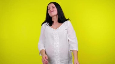 Beyaz bluzlu neşeli hamile kadın sarı arka planda gülüyor.