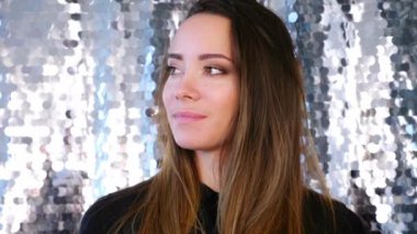 Makyajlı kadın sandalyeye oturmuş yan tarafa bakıyor ve gülümsüyor.