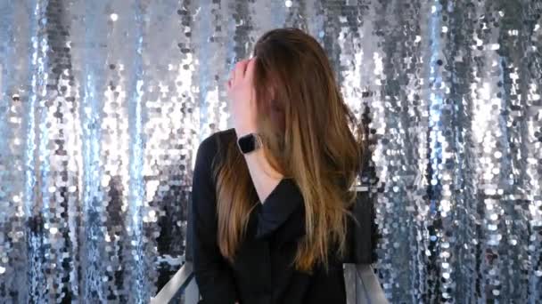 Vrouw met make-up zit op stoel en straalt haar op glanzende zilveren achtergrond — Stockvideo