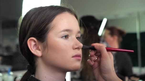 Make-up kunstenaar brengt stichting op gezicht met borstel naar tiener meisje in salon — Stockvideo