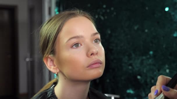 Makeup καλλιτέχνης εφαρμόζει ίδρυμα στο πρόσωπο με βούρτσα για έφηβος κορίτσι στο σαλόνι — Αρχείο Βίντεο