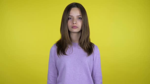 Tini lány rózsaszín pulóverben néz a kamera sárga háttér — Stock videók