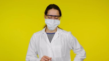Koruyucu tıbbi maskeli, gözlüklü ve beyaz önlüklü genç bir doktor.