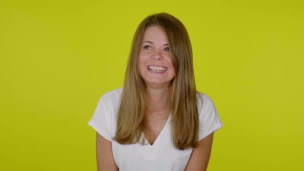 Mujer con una camiseta blanca se ríe sobre un fondo amarillo con espacio para copiar — Vídeos de Stock