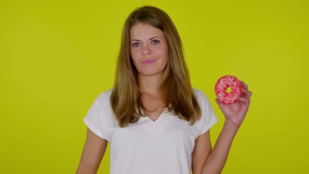 Vrouw steekt hand op met een rode donut, toont afkeer, grimmig op gele achtergrond — Stockvideo