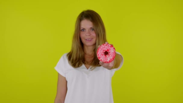 Mulher de t-shirt levanta a mão com um donuts vermelho na câmera, sorri — Vídeo de Stock