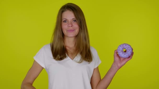 Woman in a white T-shirt raises hand with a blue donuts, shows like, smiles — Stock Video