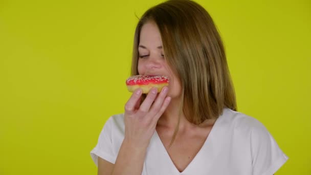 Frau im weißen T-Shirt beißt zu, isst geschmacklose rote Donuts, ärgert sich über Geschmack — Stockvideo