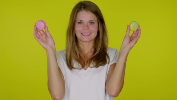 Femme ferme, ouvre les yeux en jaune, macarons roses, tient macarons dans les mains, sourit — Video