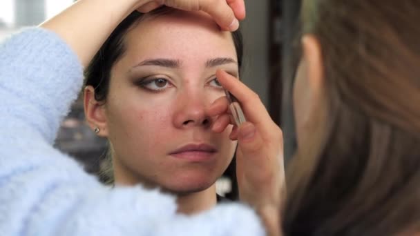 Maquillaje artista pinta sombras de ojos con lápiz a mujer joven en salón de belleza — Vídeos de Stock