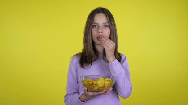 Tini lány eszik burgonya chips üveg tál sárga alapon — Stock videók