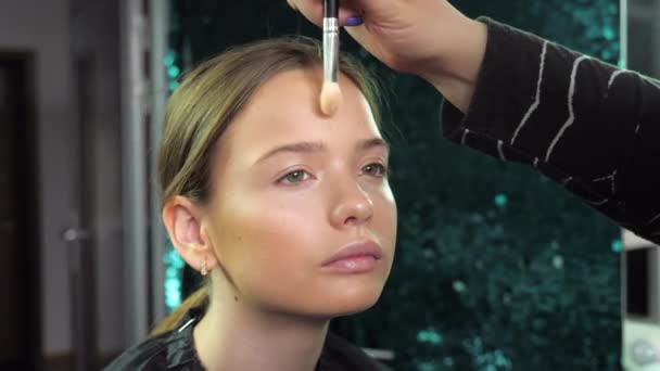 Make-up umělec aplikuje prášek na obličej štětcem na dospívající dívku v salonu — Stock video