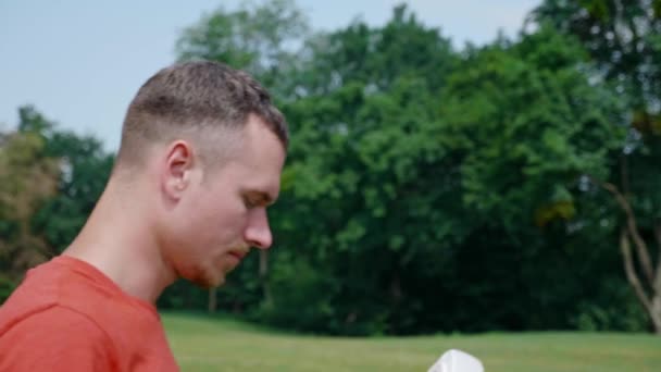 Homem em um parque em uma camiseta vermelha coloca um capacete realidade virtual na cabeça — Vídeo de Stock