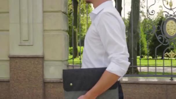 Homme d'affaires avec un ordinateur portable dans la main marche à travers le parc — Video