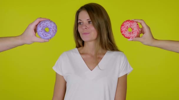 Donna in maglietta bianca si guarda intorno e non riesce a decidere quale ciambella mangiare — Video Stock
