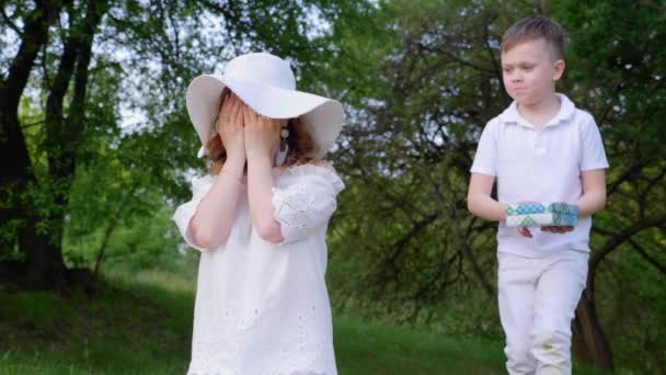 Γιος σε λευκό παντελόνι και t-shirt δίνει μαμά σε ένα λευκό κουτί καπέλο με δώρο — Αρχείο Βίντεο
