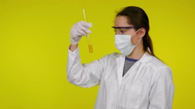 Beyaz elbiseli kadın, koruyucu maske test tüpünün içindekileri inceliyor.