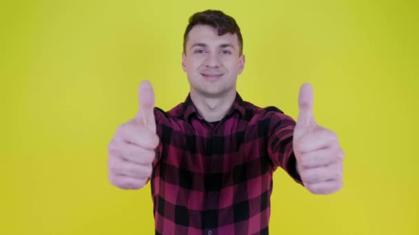 Ο άνθρωπος με το ροζ καρό πουκάμισο χαμογελά, σηκώνει το χέρι και δείχνει όπως στο κίτρινο φόντο — Αρχείο Βίντεο