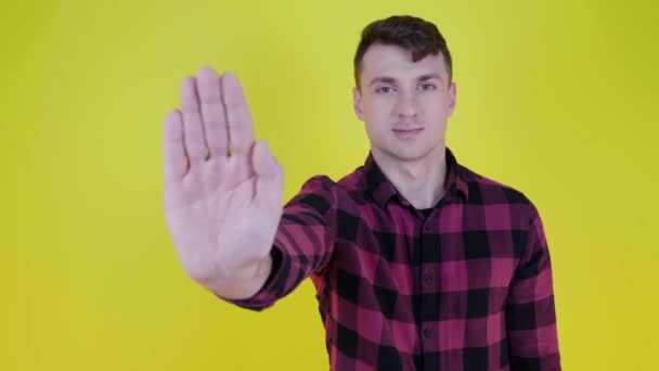 Человек поднимает руку, показывает ладонь к камере и говорит стоп на желтом фоне — стоковое видео