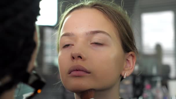 Make-up umělec aplikuje základ na tvář se štětcem na dospívající dívku v salonu — Stock video