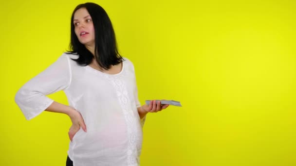 Riche femme enceinte se tient avec un paquet d'argent à la main sur un fond jaune — Video