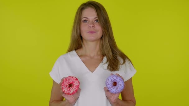 Vrouw in een wit T-shirt draait blauwe en rode donuts op de borst en glimlacht — Stockvideo