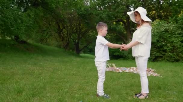 Ibu, anak berpegangan tangan dan berputar. Perempuan, anak kecil bermain di taman di rumput hijau — Stok Video