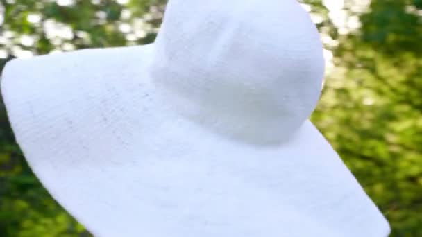 Κοντινό πλάνο γυναίκα σε ένα λευκό καπέλο κοιτάζει γύρω στο πάρκο σε ένα φόντο των δέντρων — Αρχείο Βίντεο